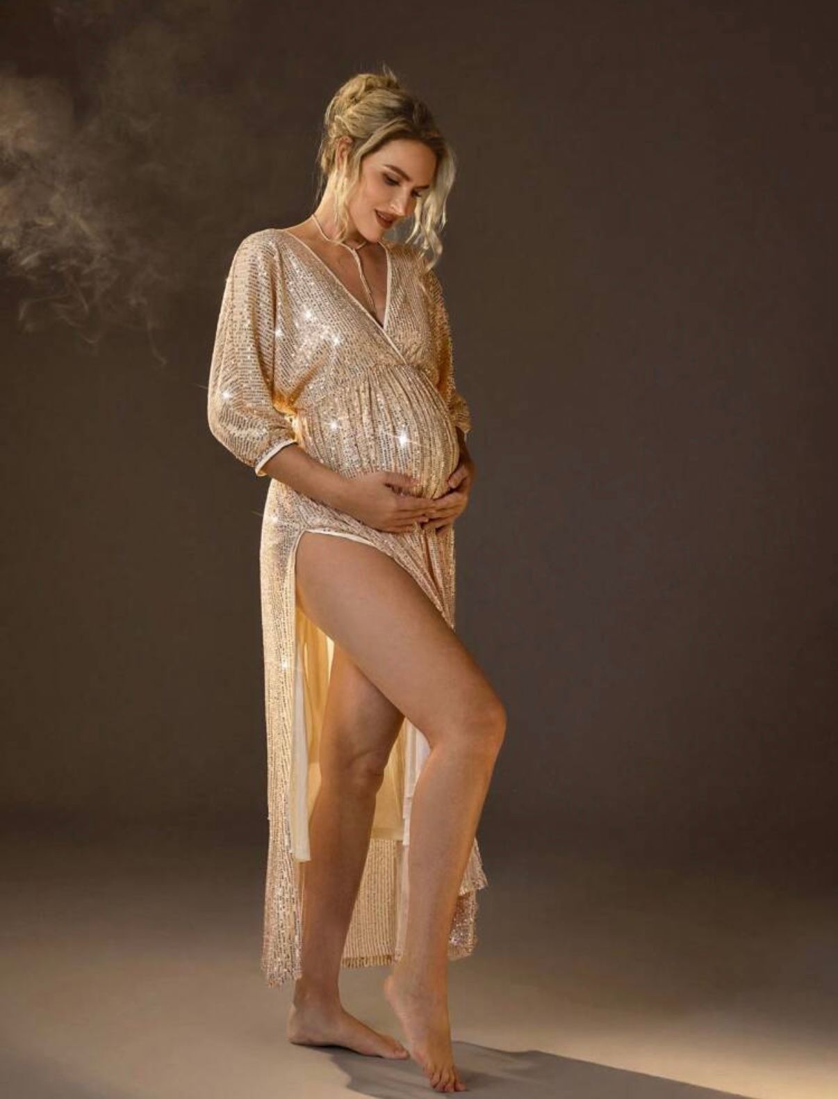 Sparkly champagne-colored maternity gown with long sleeves in moody lighting.