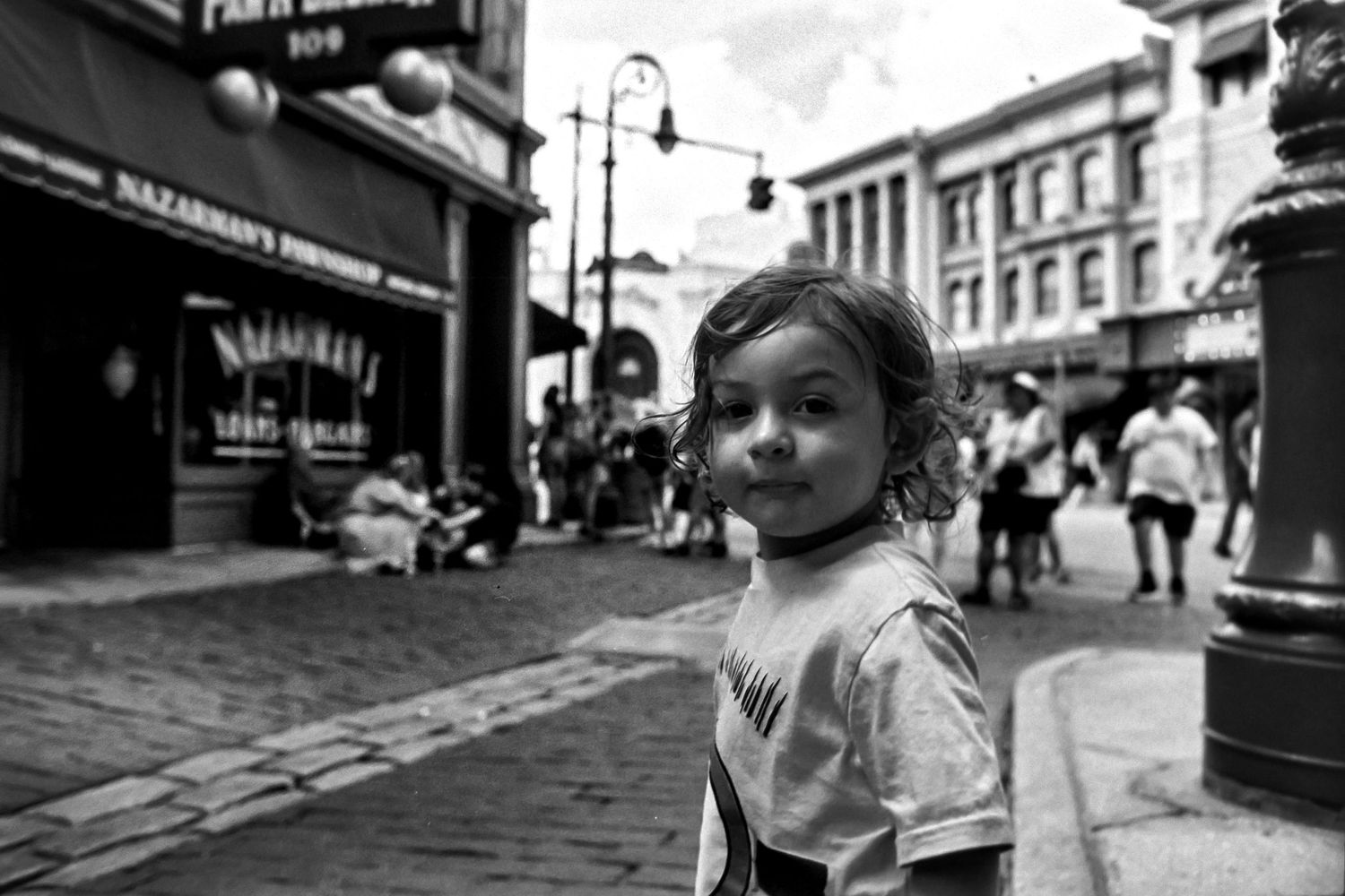 A black and white street scene shows a figure in foreground with historic buildings and pedestrians in the background.