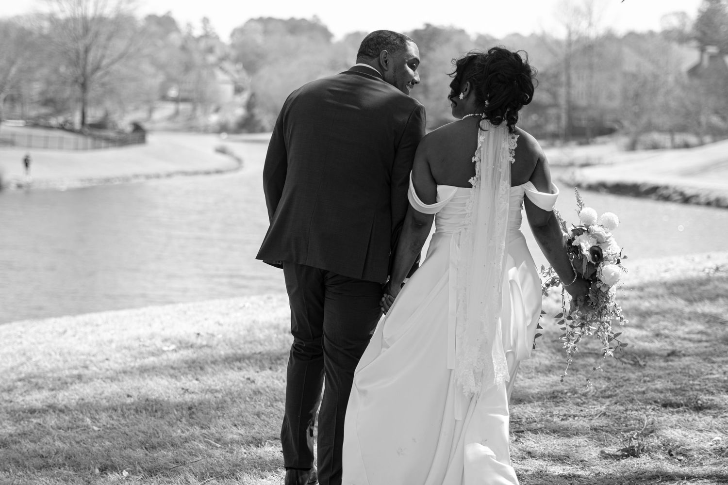 Newlywed couple walking together by a lake in a scenic black and white wedding photo.