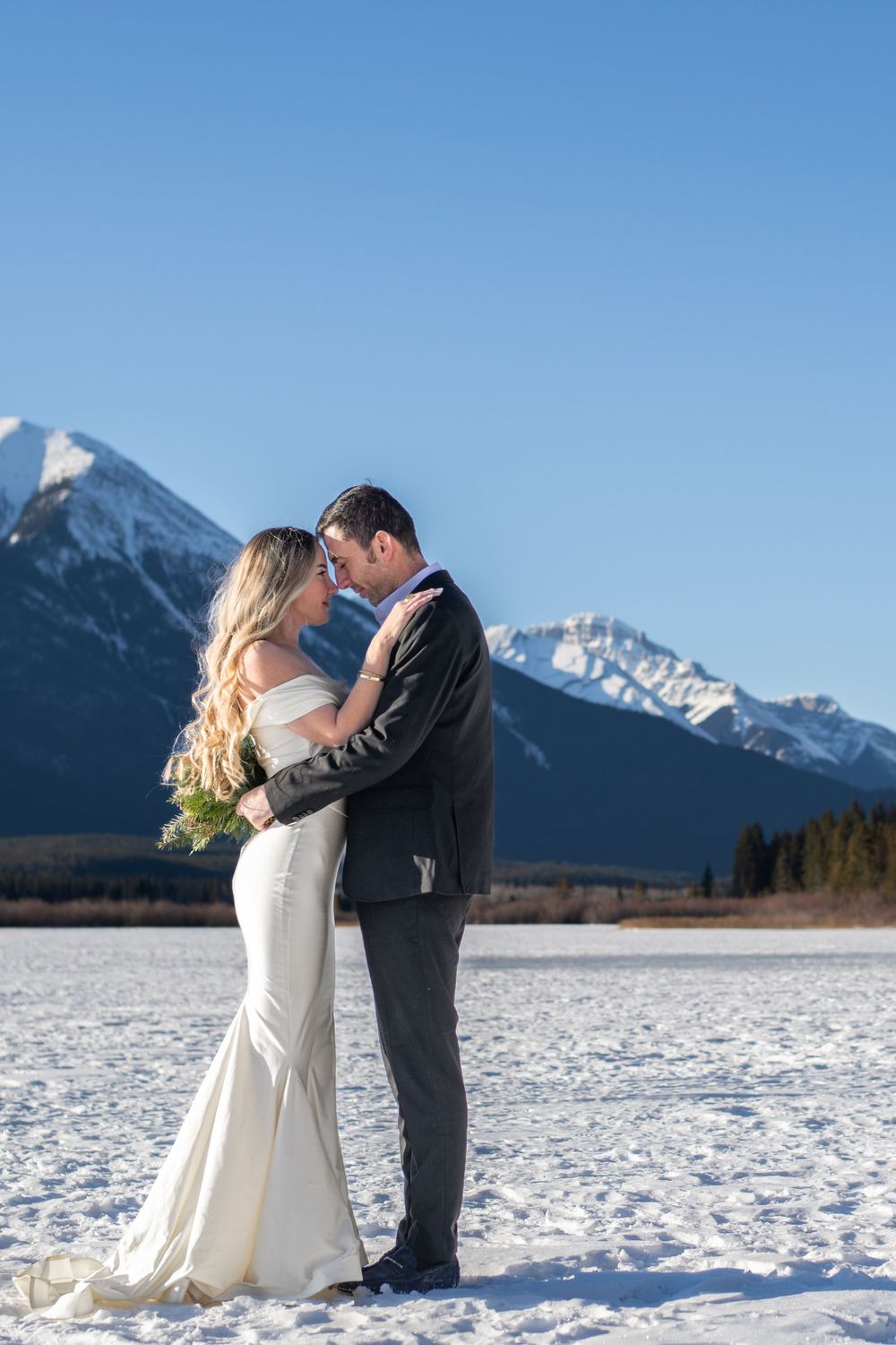 Romantic winter wedding photos with couple embracing in snowy mountain landscape.