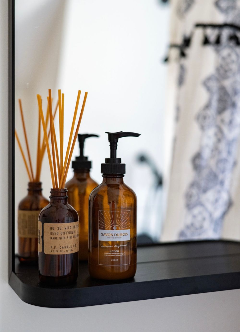 Collection of amber glass reed diffusers and fragrance bottles displayed on dark shelf.