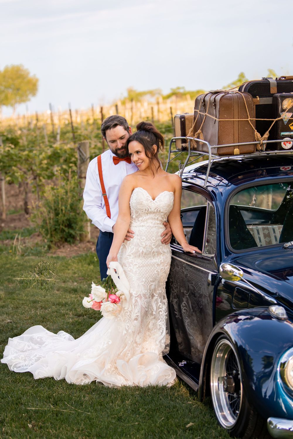 Elegant wedding photoshoot with a classic blue car in an outdoor vineyard setting.
