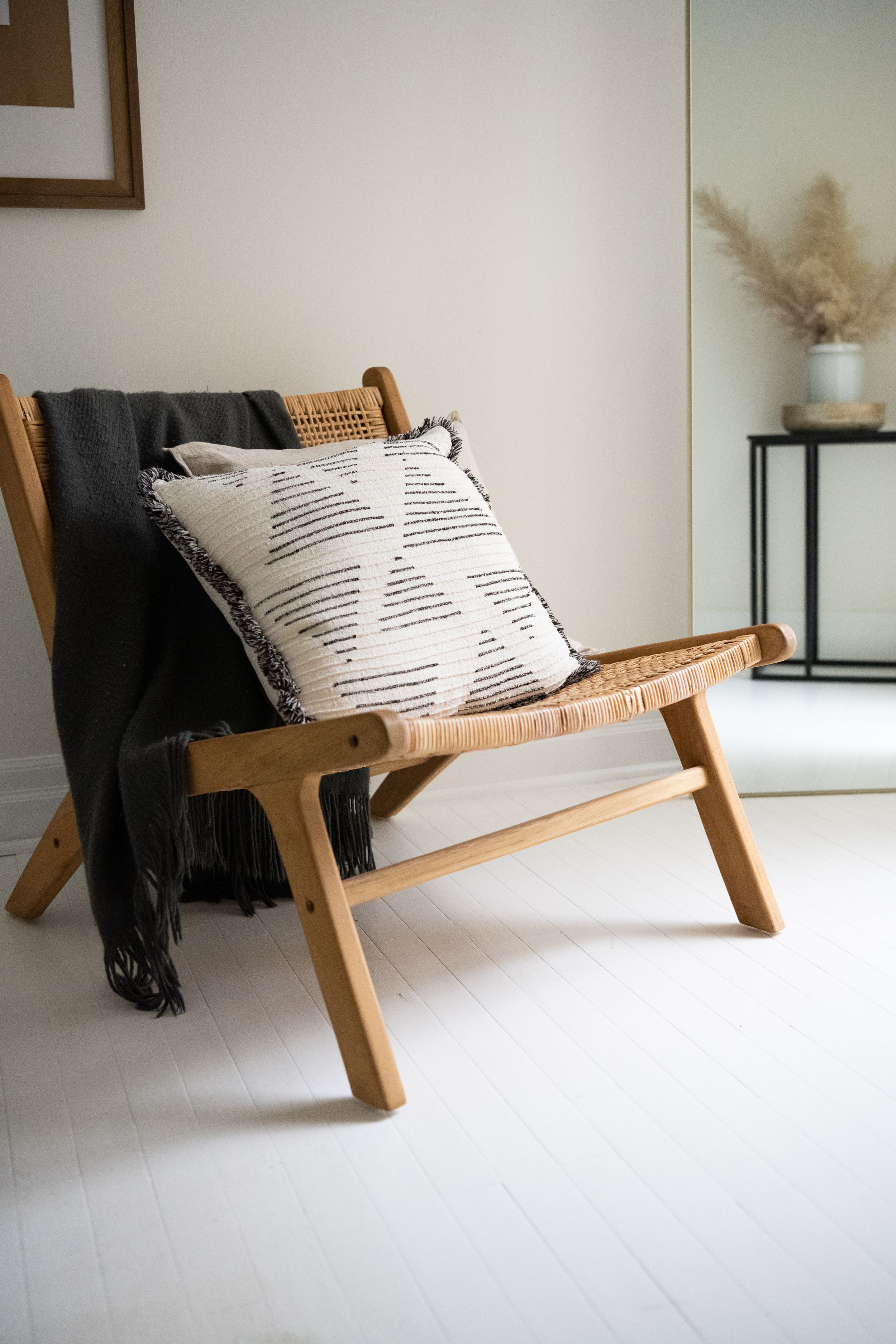 Modern wooden lounge chair with striped pillows and black throw blanket in minimalist setting.