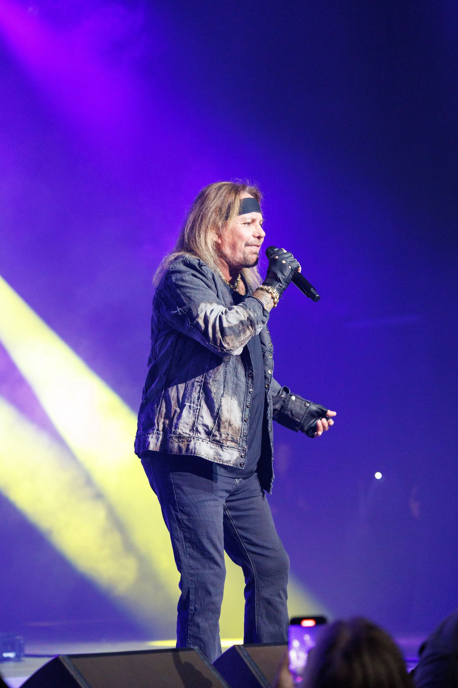 Singer performing on stage in denim outfit under purple and yellow concert lighting.