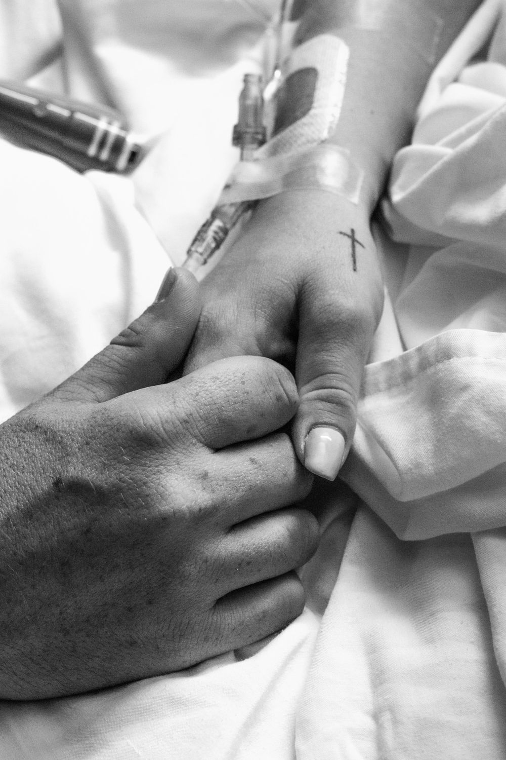 Black and white medical image showing IV line being inserted into a patient's hand with medical staff assistance.
