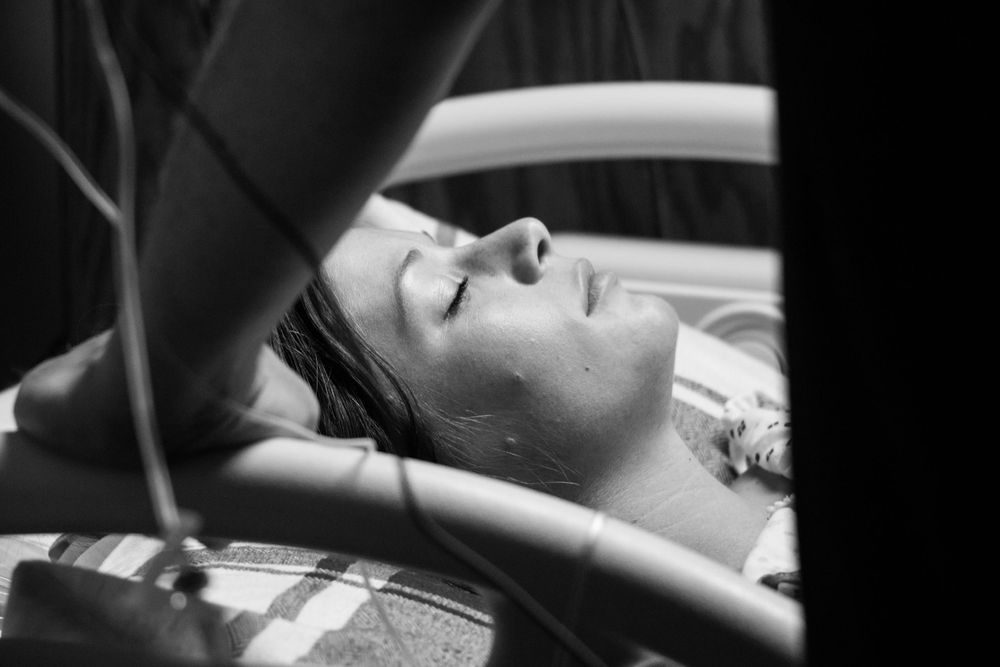 A black and white portrait of someone asleep or resting peacefully in a car, photographed through the window.