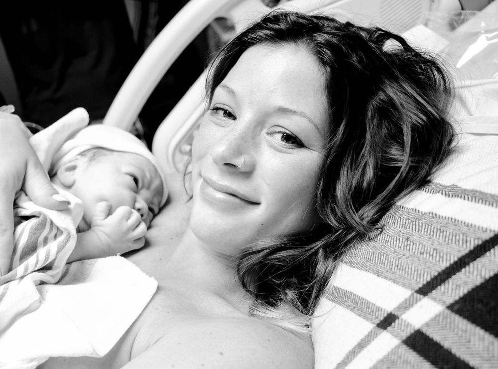 Black and white photograph showing someone smiling warmly while resting with a sleeping baby.