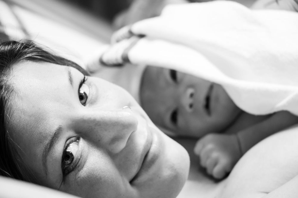 Black and white photo of parent and baby lying in bed together, shot in close soft focus.