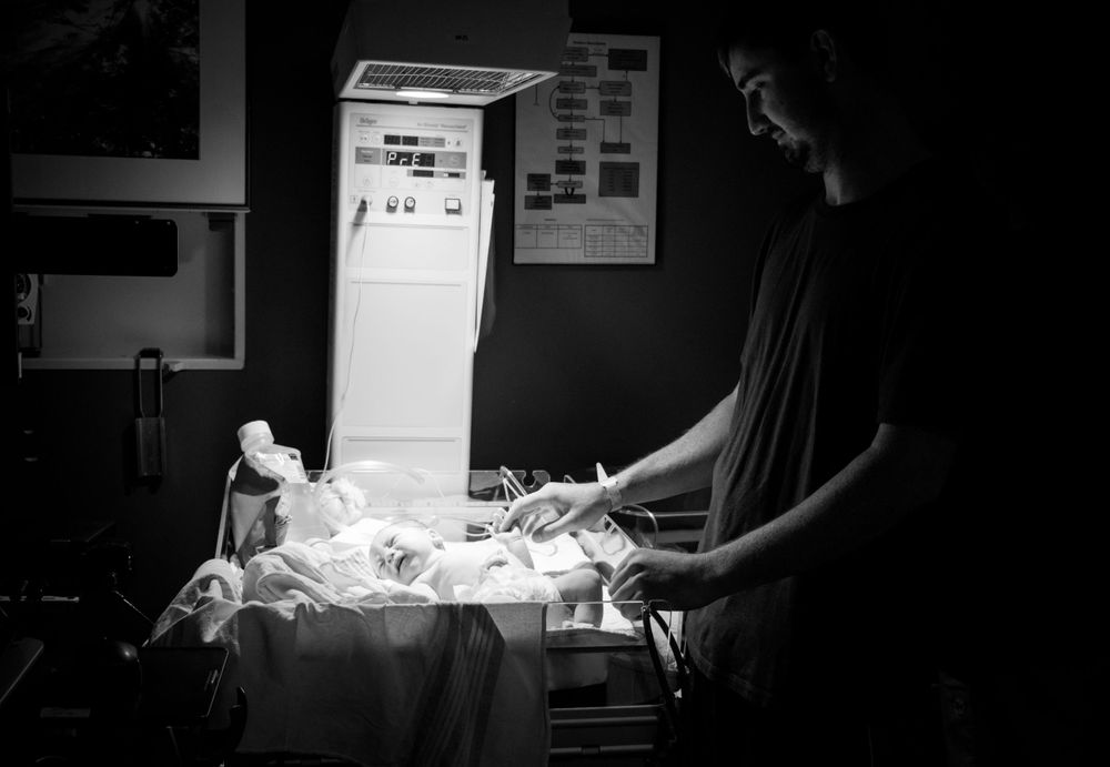 Medical professional attending to a newborn infant under a warming light in a black and white hospital photograph.
