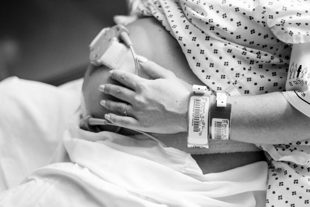 Black and white close-up of a hospital patient's arm with medical identification bracelets resting on white bedding.