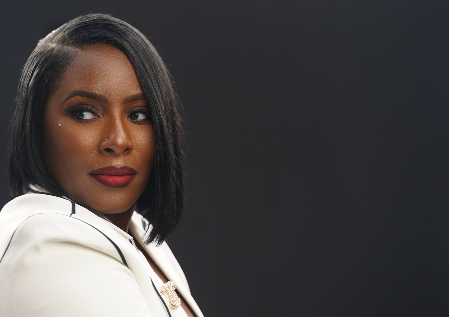 Professional portrait against dark background featuring elegant white blazer and red lipstick.