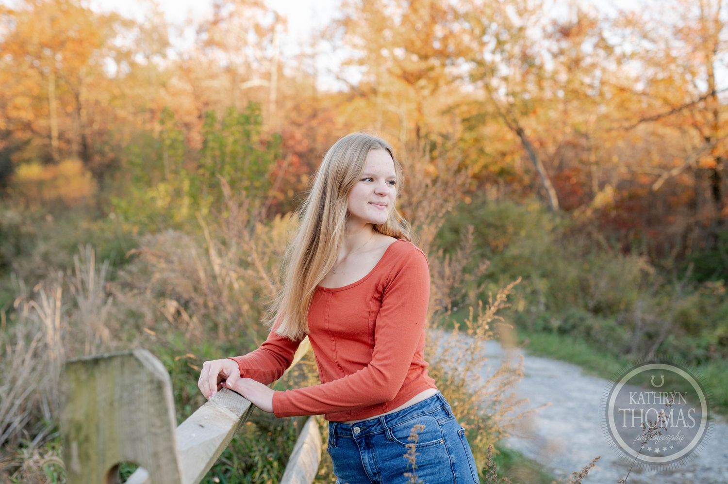 Outdoor portrait along a wooden fence with golden autumn foliage creating a warm backdrop.