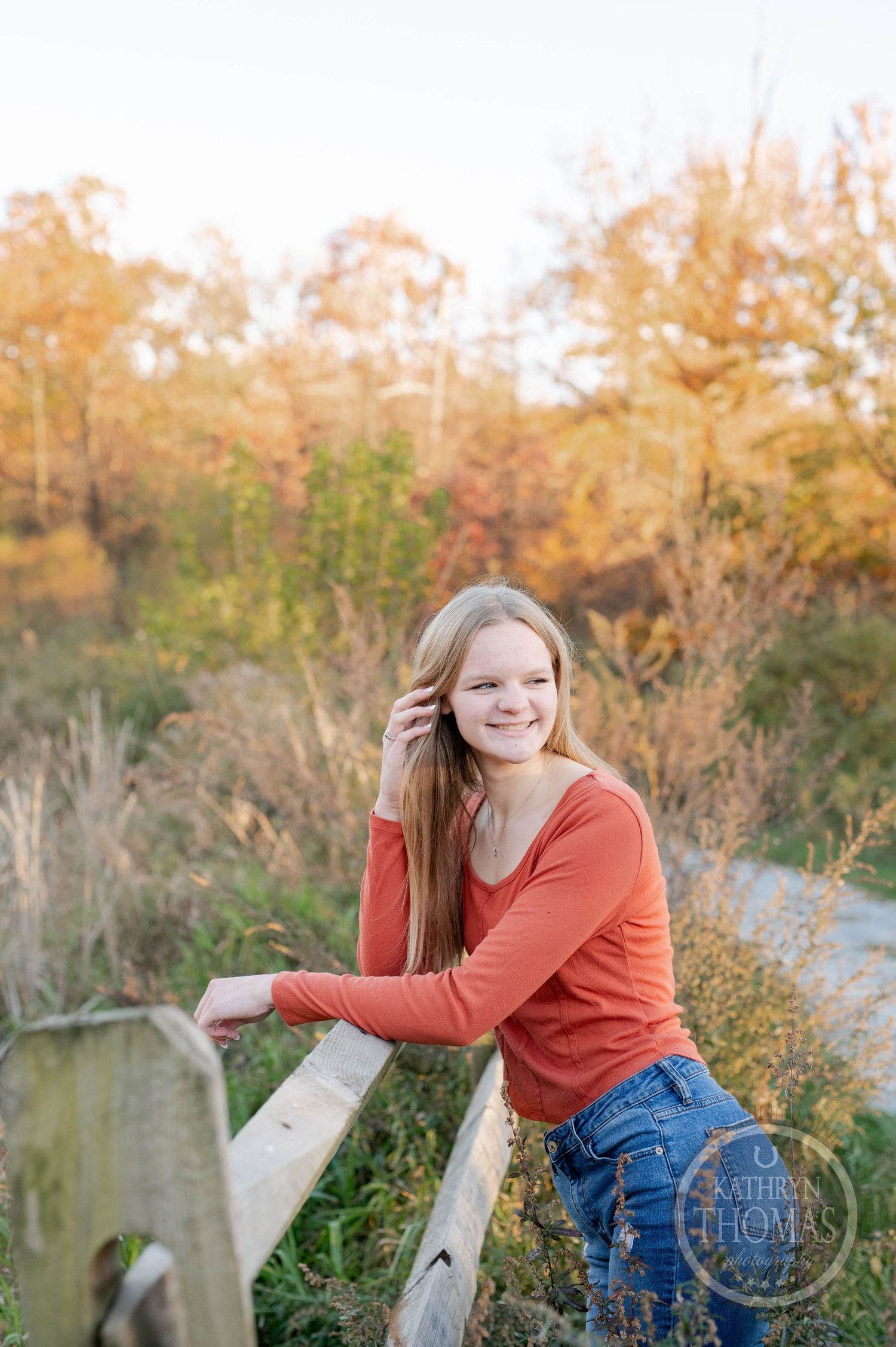 Natural outdoor portrait by a wooden fence with fall colors and foliage in the background.