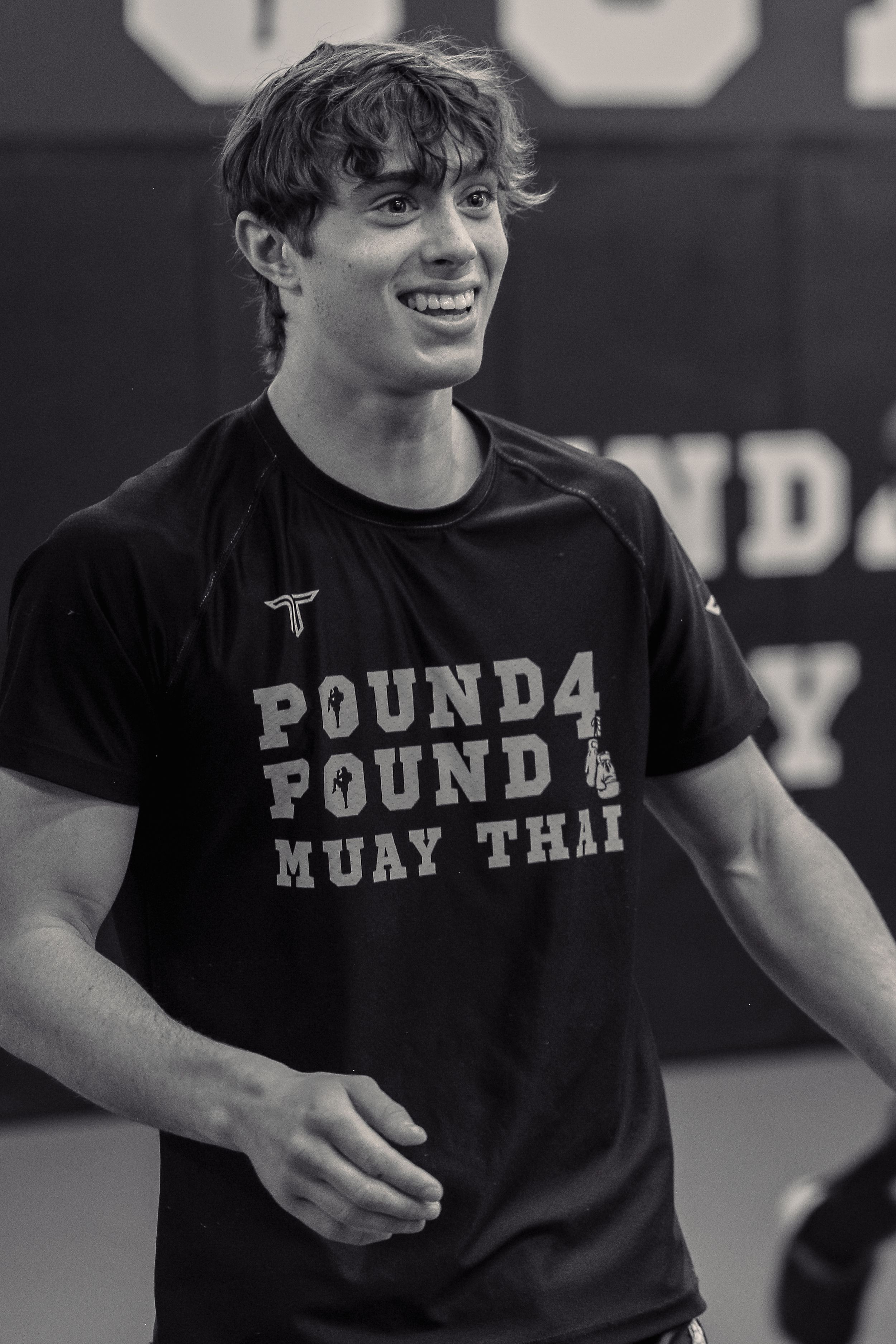 Athlete wearing a black Pound4 Pound Muay Thai t-shirt smiles during training session in black and white photo.