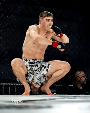 MMA fighter in black and white patterned shorts crouches in fighting stance during match in octagon cage.