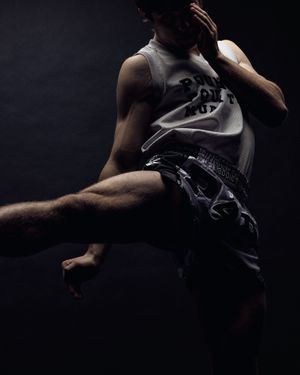 A dancer in black athletic wear leaps gracefully against a dark background, displaying dynamic movement and strength.