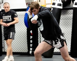 MMA fighter in black hoodie and shorts practices shadow boxing technique during training session in gym.