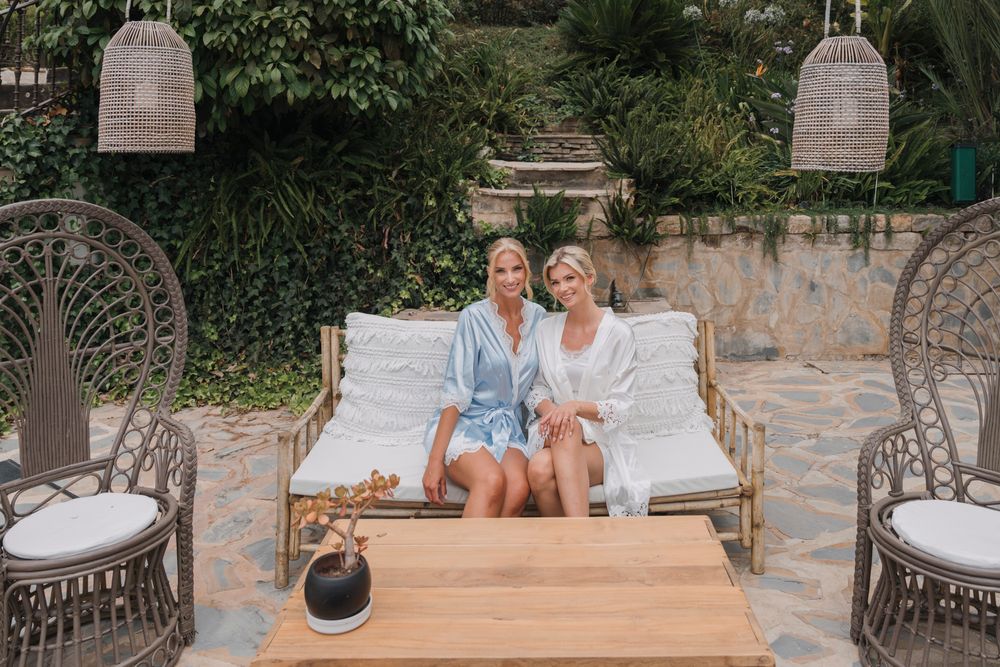 Two people relaxing on an elegant outdoor lounge setup with wicker chairs and white cushions.