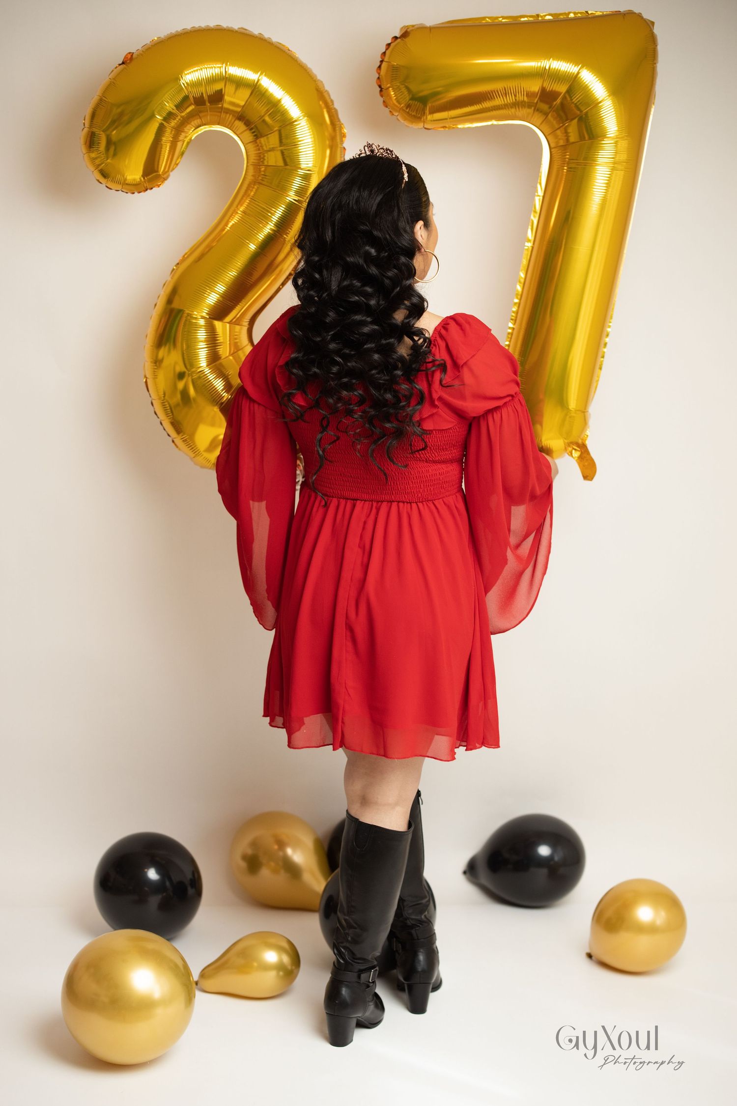 Red dress and black boots Vintage-inspired birthday photoshoot with golden number 27 balloons and decorative gold and black spheres.