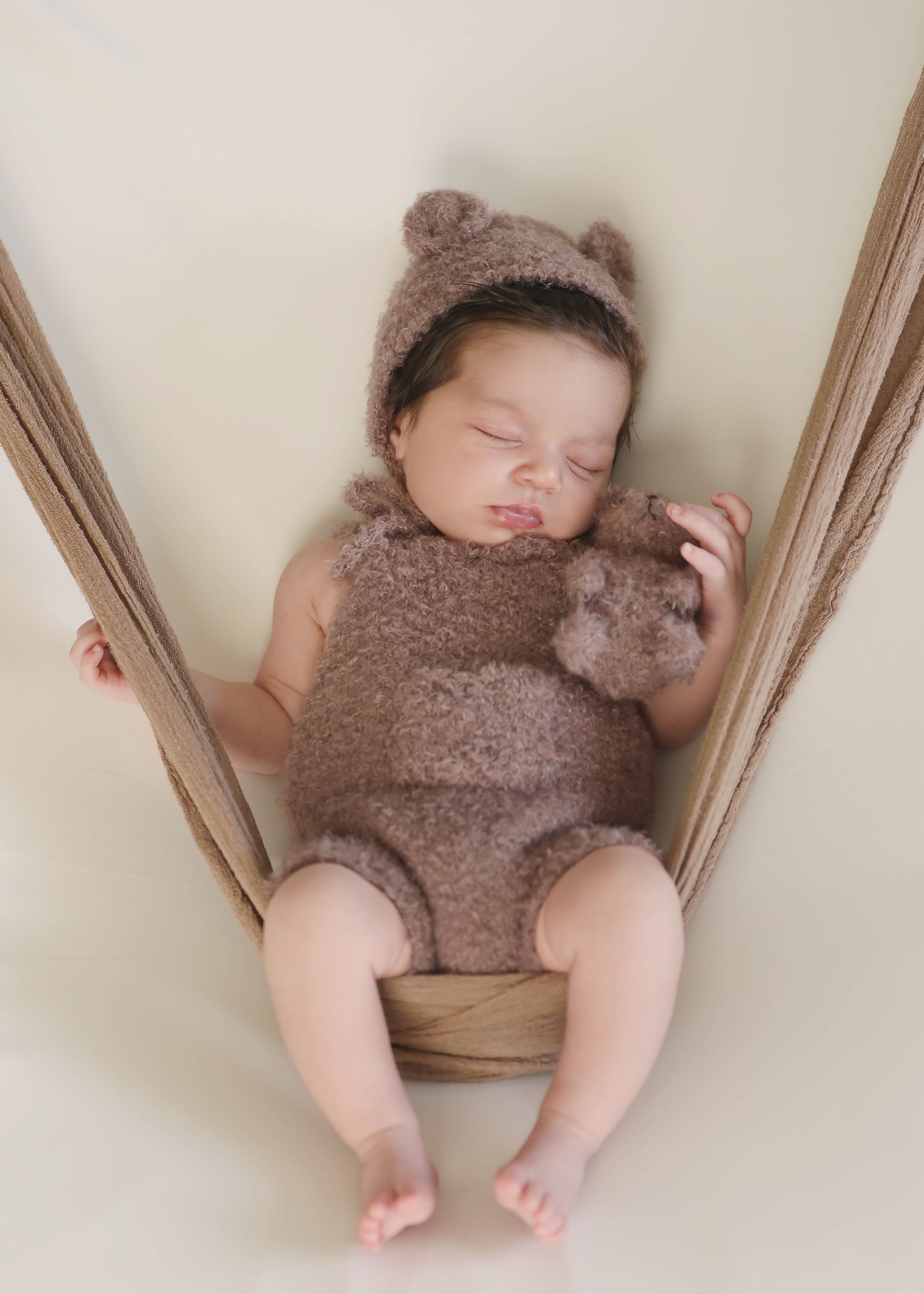 Baby wearing brown teddy bear outfit lying on wooden surface.