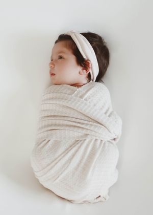 Newborn baby wrapped in white textured blanket on light background.