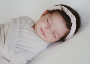 Sleeping baby in white headband and wrap against light background.