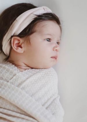 Side profile of sleeping newborn wearing white headband and wrap.