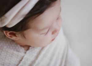 Detail shot of sleeping baby with white headband against light background.