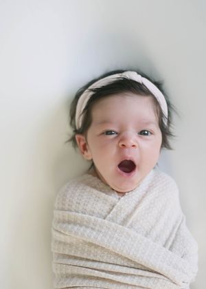 A newborn baby wrapped in a white knit blanket makes various facial expressions in a series of photos.