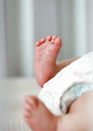 Close-up of a newborn baby's tiny feet wearing a white diaper, with soft focus background.