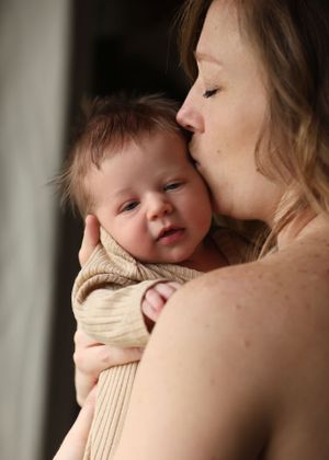 A tender moment between parent and baby in soft natural light with the infant wearing a beige knit sweater.