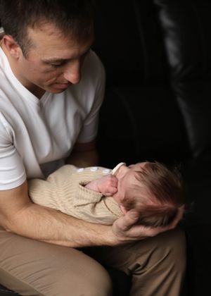 An intimate portrait of a parent cradling a newborn baby wearing a cream-colored sweater.