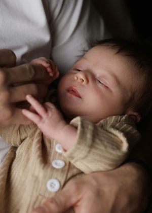 A sleeping infant in a cream cardigan being gently held against a white shirt.