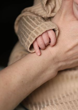 Close-up of a tiny baby hand grasping from inside a beige knitted sleeve.