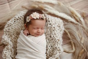 Peaceful newborn portrait with lace headband on textured cream blanket.