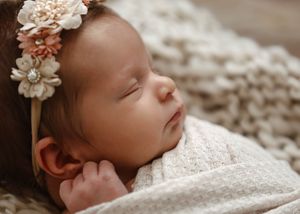 Close-up of sleeping newborn with floral crown wrapped in white swaddle.