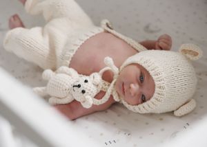 A newborn wearing a white knitted bunny outfit lying peacefully.