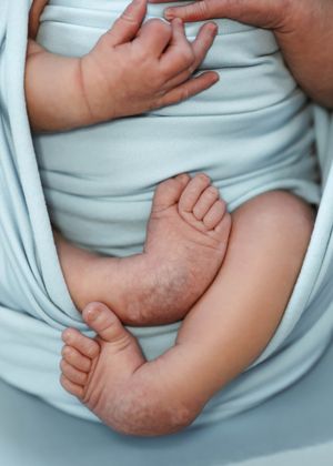 Close-up series of a swaddled newborn's tiny feet and hands against a light blue background.
