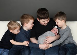 Series of children laying in a row on grey background showing sibling connection.