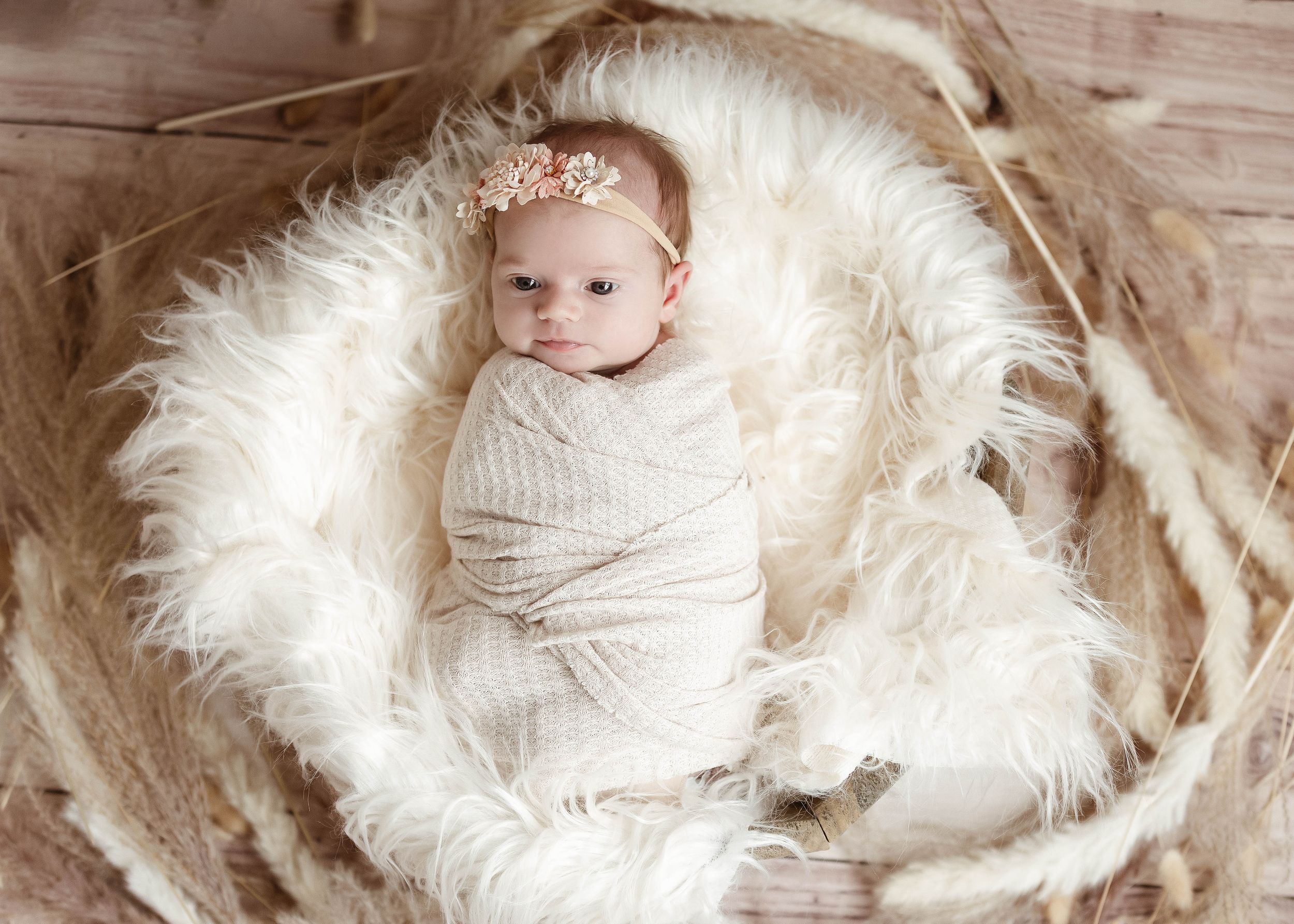 Progression of newborn photos on white furry backdrop with rustic wooden elements.