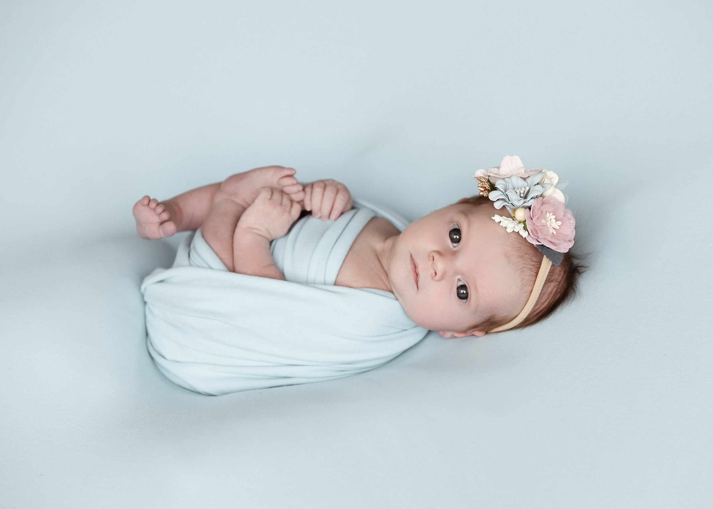 A newborn baby wearing white lies peacefully against a light blue background.