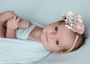Gentle newborn portraits with floral headpiece against soft blue background.