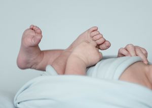 Close-up details of tiny baby feet and legs on a light background.