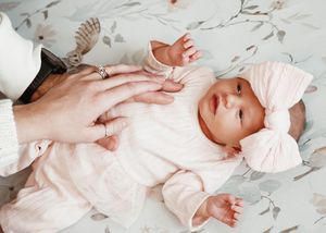 A newborn baby wearing soft pink clothing lies on white fabric in a series of gentle poses.