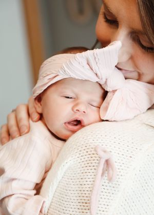 Baby in pink clothing rests peacefully against a mothers shoulder.