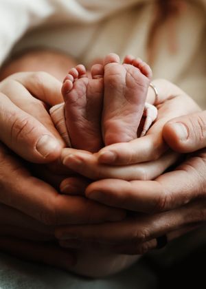 Tiny newborn feet and hands held gently in caring palms.