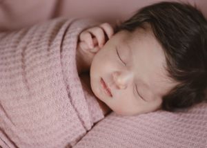 A baby lies on pink fabric making different expressions while swaddled in white.