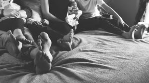 Black and white photo of a family relaxing together on a bed, with baby feet and children visible.