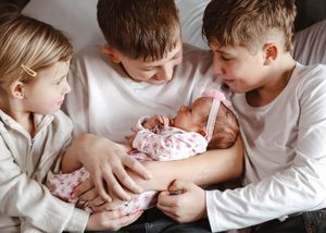 Three siblings lovingly hold and admire their newborn baby, sharing a tender family moment together.