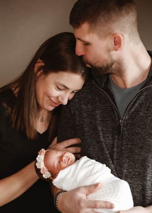 A couple tenderly gazes at their newborn baby wrapped in white, capturing a precious family portrait moment.